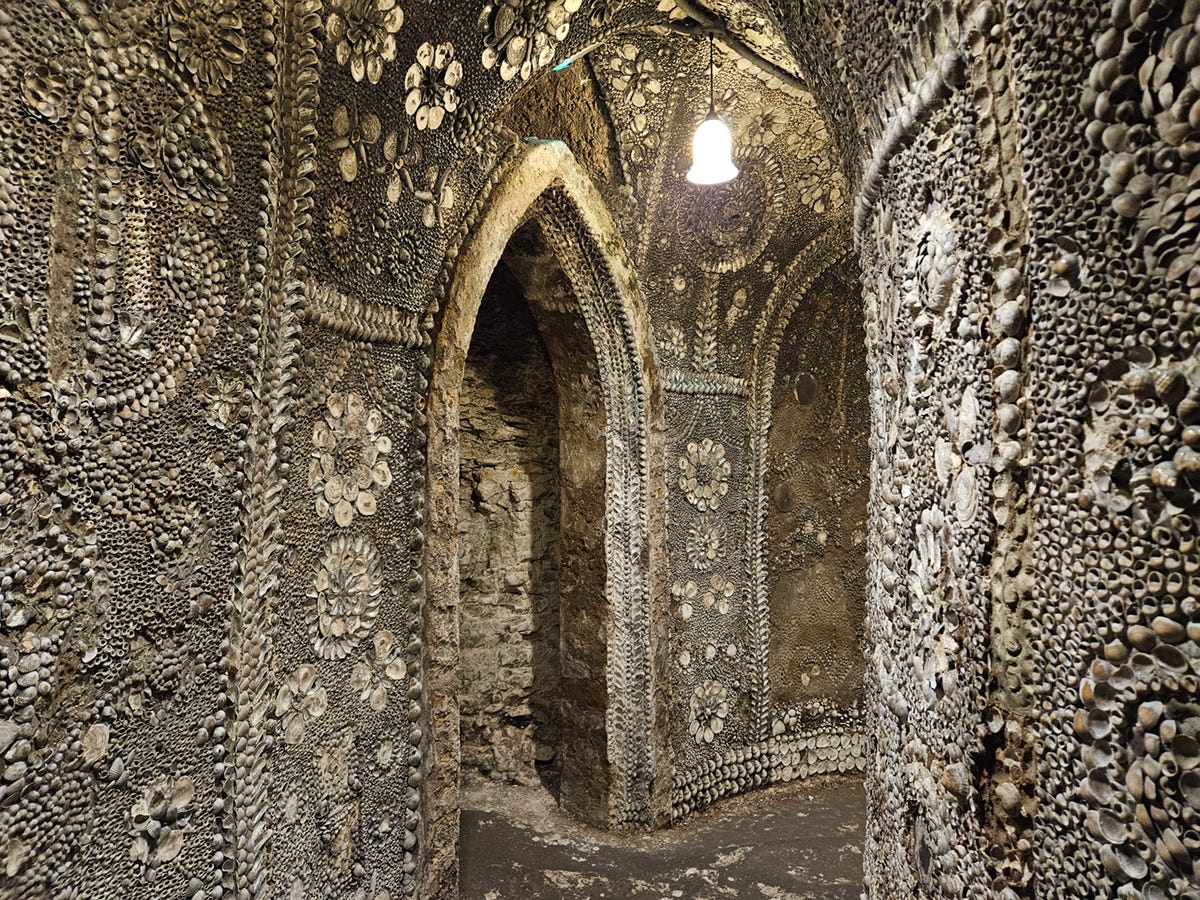 A curved passageway with an arched door leading off it. The walls and ceilings are covered in shells