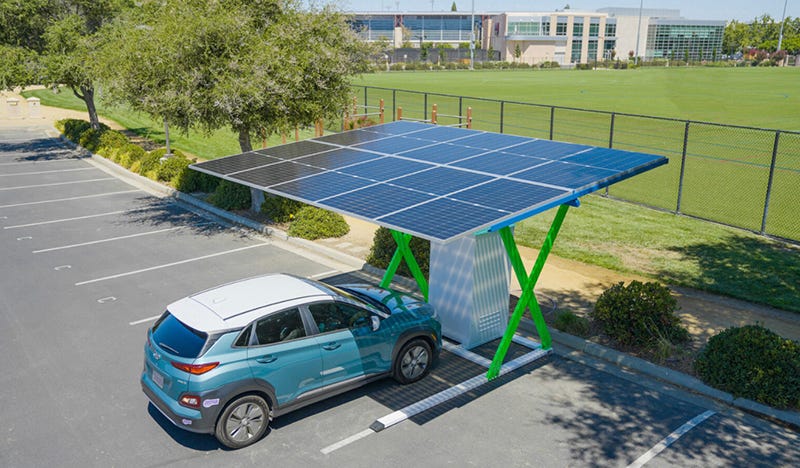An EV charging under a single-parking space solar panel system in a parking lot near a school or other business