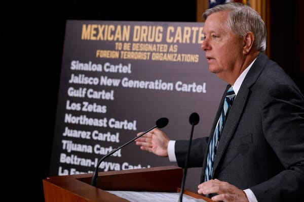 Senator Lindsey Graham stands at a podium, gesturing to a placard next to him listing Mexican drug cartels.