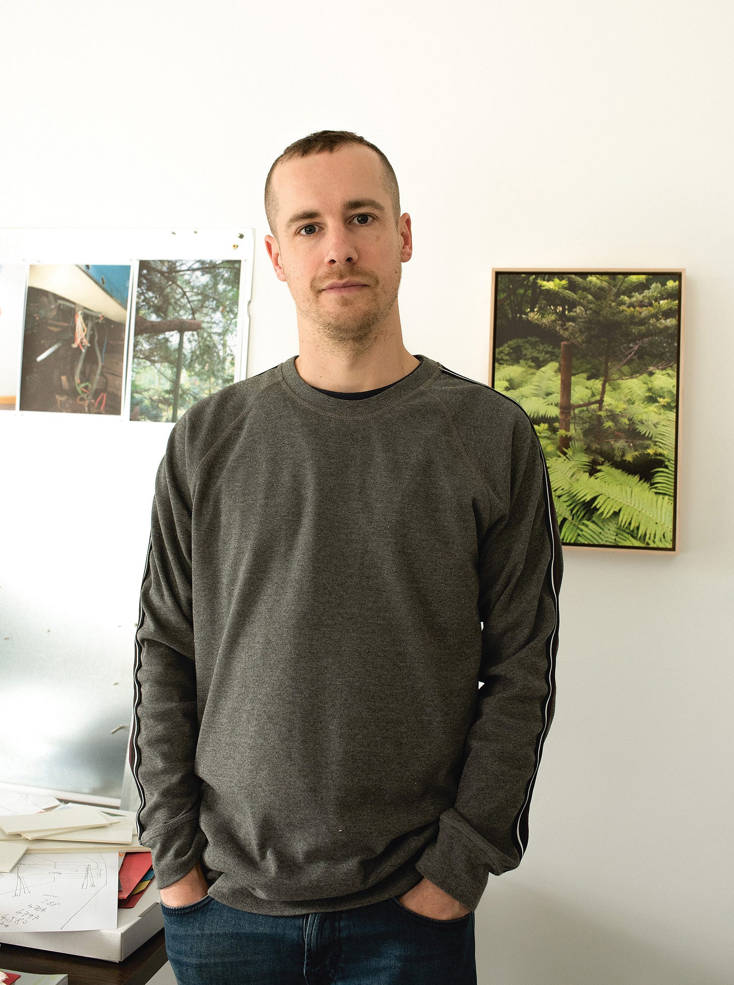 Rob Crosse standing in his studio with photos of woodland on the walls behind him