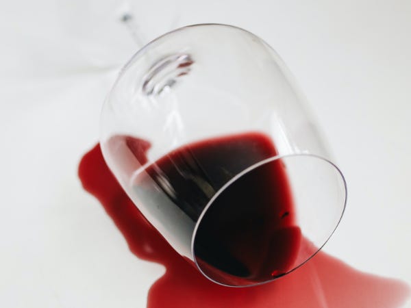 Wine glass on its side spilling red wine all over a white surface