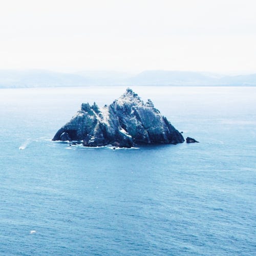 An image of a rocky island in the distance. Blue hue.