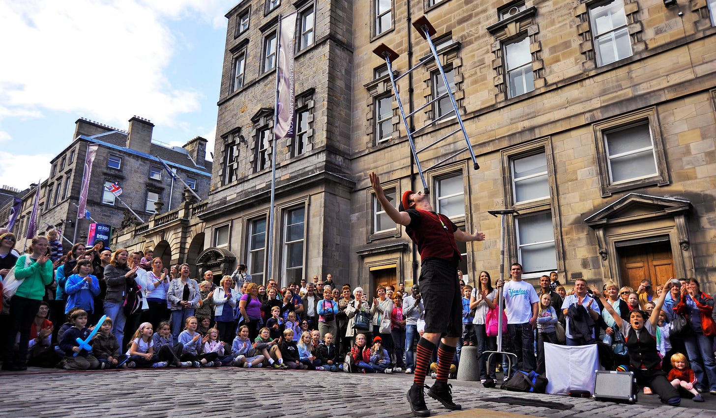 A street performer balances a ladder on his chin while a crowd watches