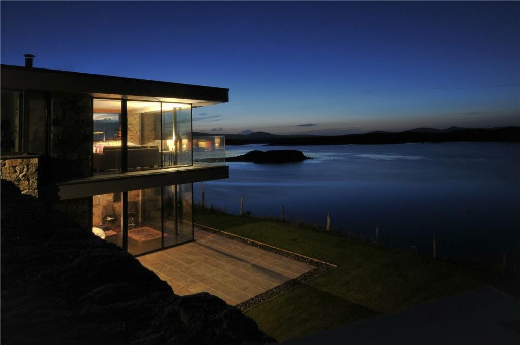 A nighttime shot of a double storey glass fronted home looking out over the loch
