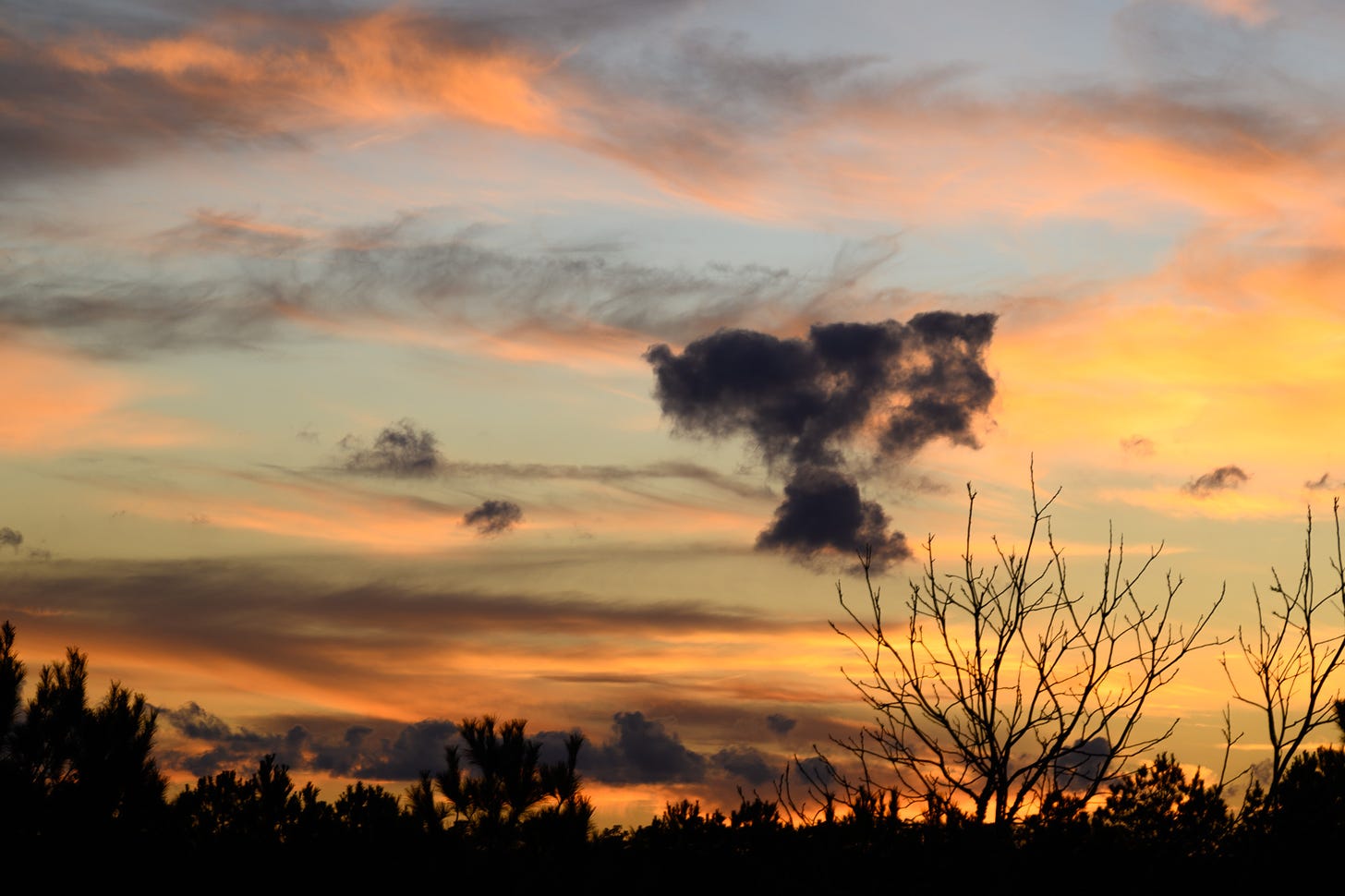 A peachy, blue, and yellow sunset against a pale blue sky with one dark mushroom shaped cloud in the center