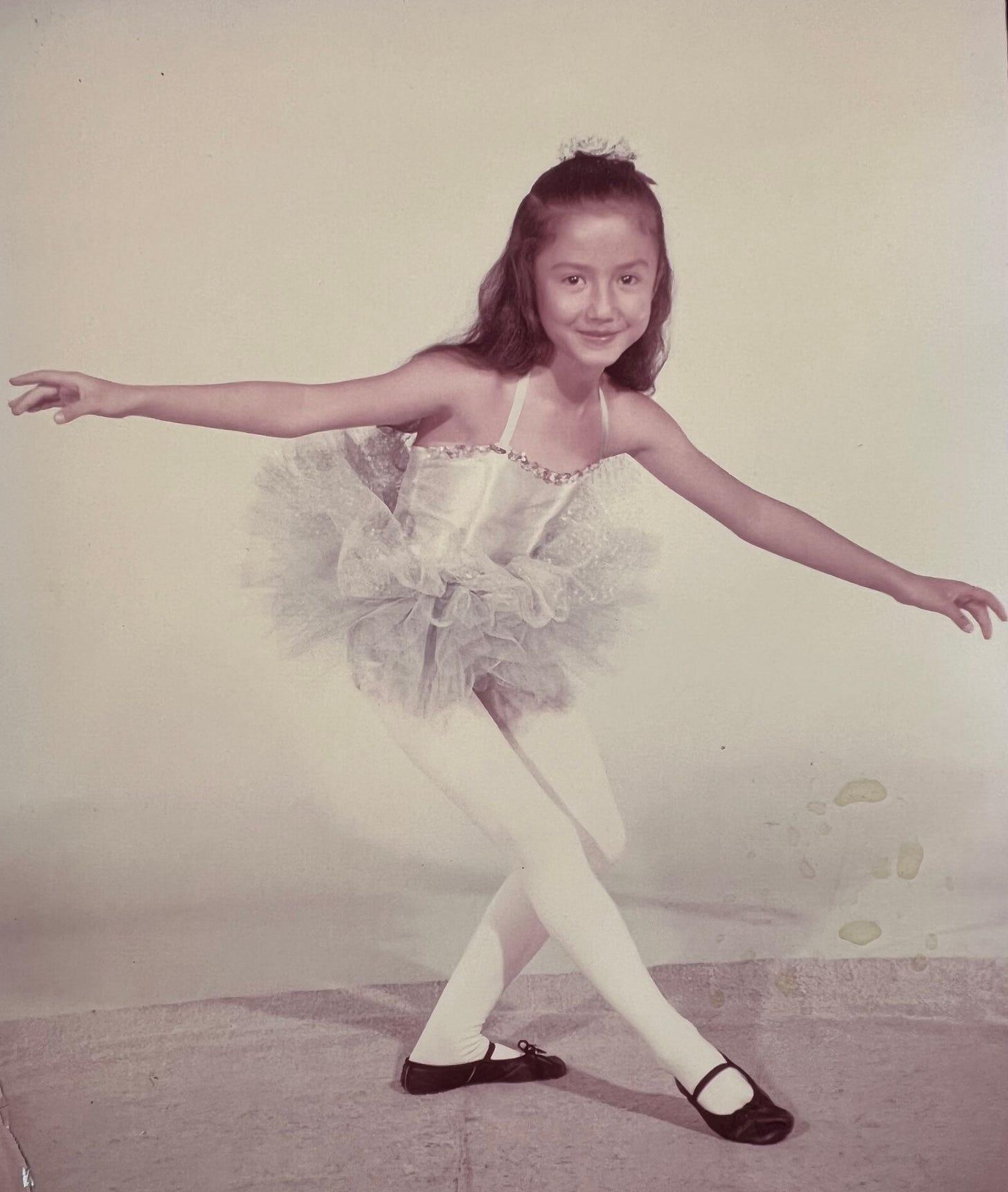 Demian, around 7 or so years old, in a silver ballerina costume with tutu, doing a ballet bow with a sparkle of happiness in her eye.