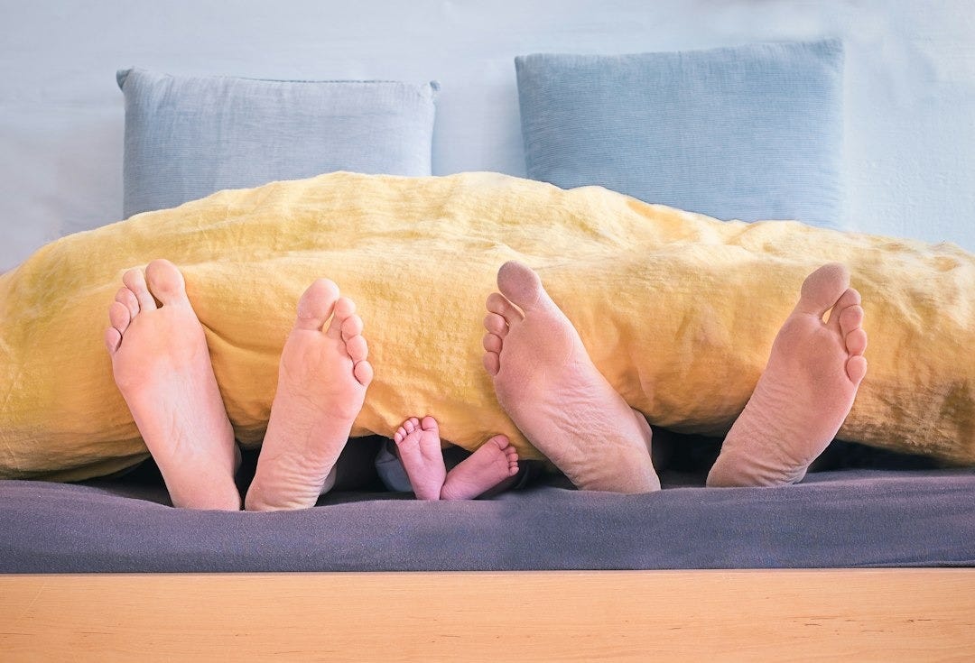 three people underneath yellow bed blanket