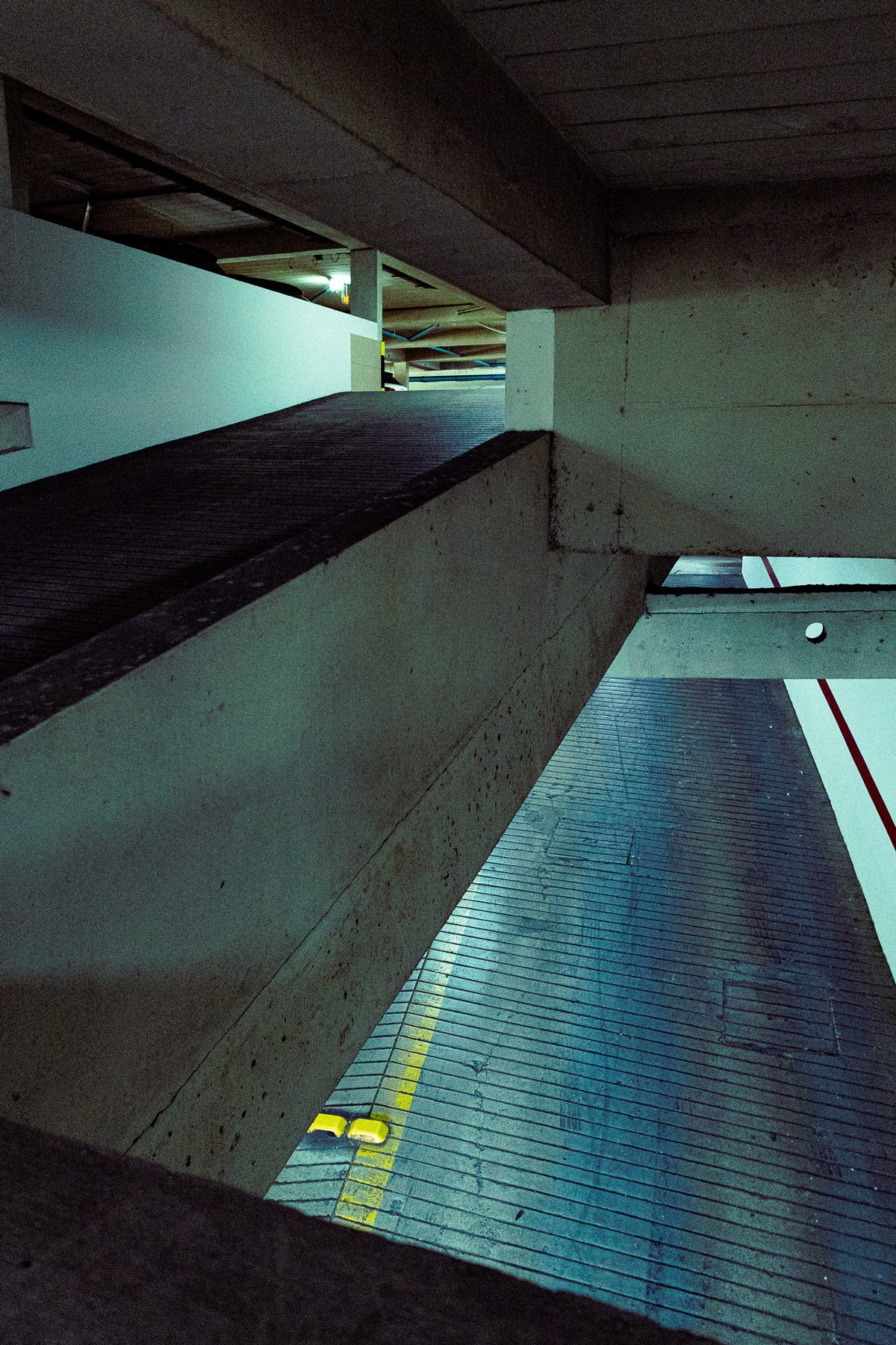 Fotografia em perspectiva de um estacionamento no segundo andar de um prédio. A imagem retrata o concreto, valorizando a iluminação, linhas e sombras.