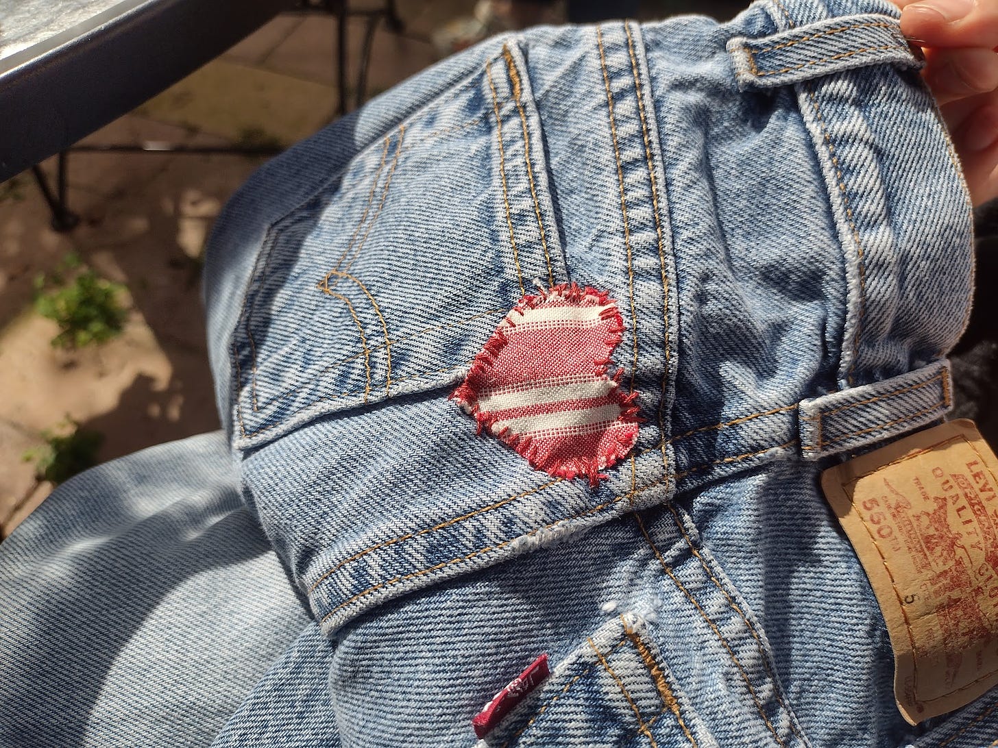 Faded jeans with a red and white heart shaped patch sewn over the top corner of a back pocket.