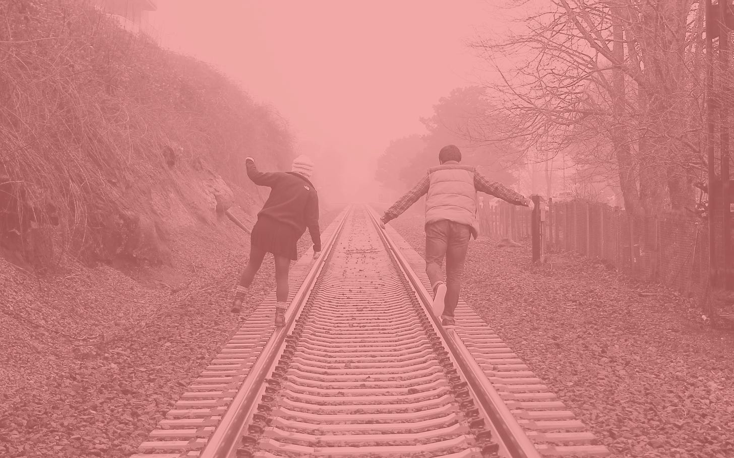 photo of two people with backs to camera balancing on railroad tracks