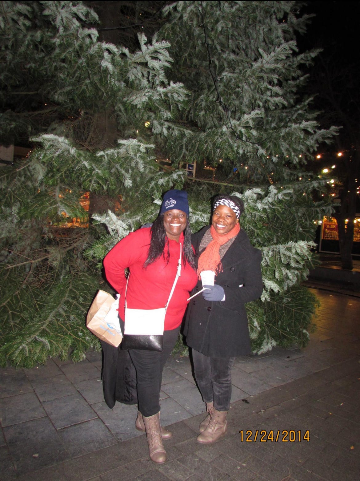 Two black women smilling and posing in front of a free with snow resedue at night in Amsterdam