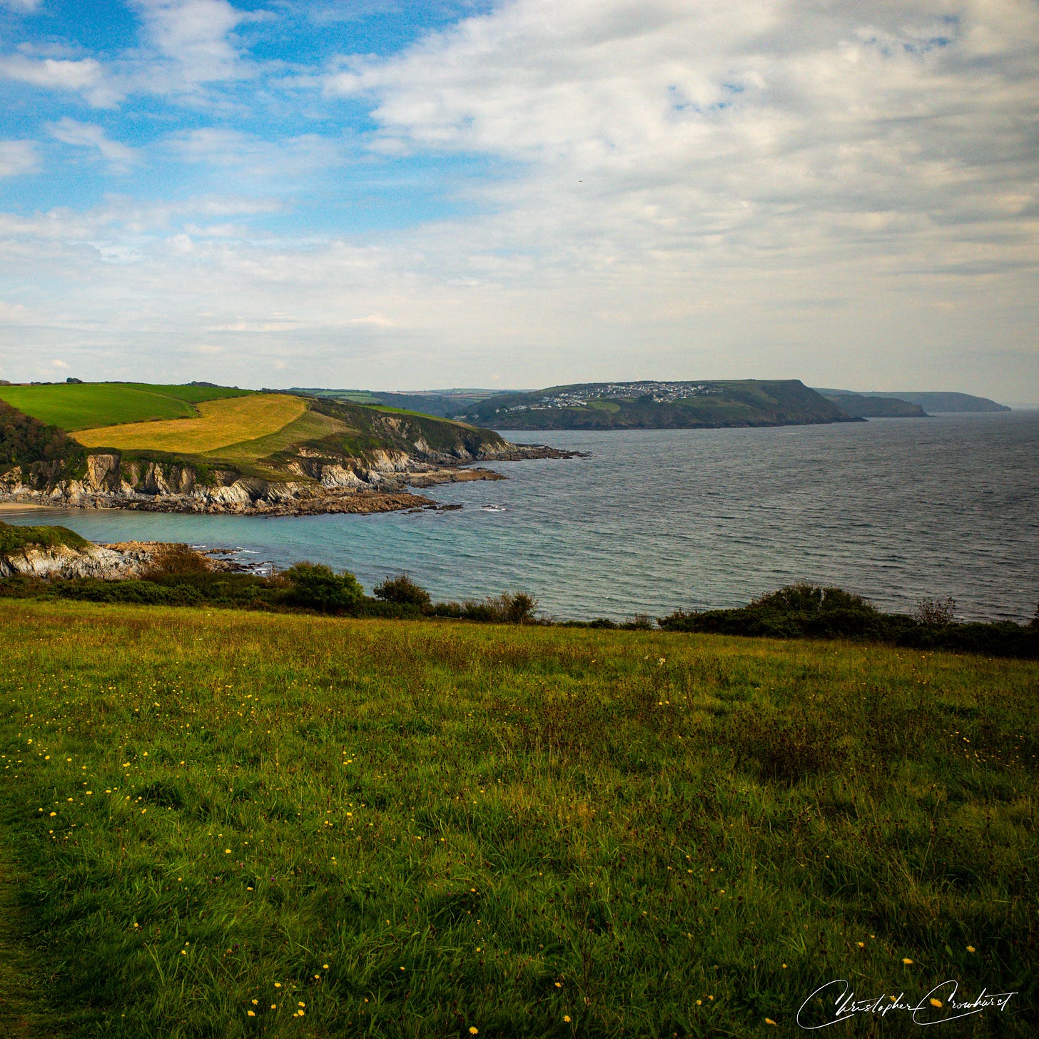 The mouth of the Fowey River estuary viewed from the Southwest Coastal path, shwoing the sea, and green field and cliffs in the distance.