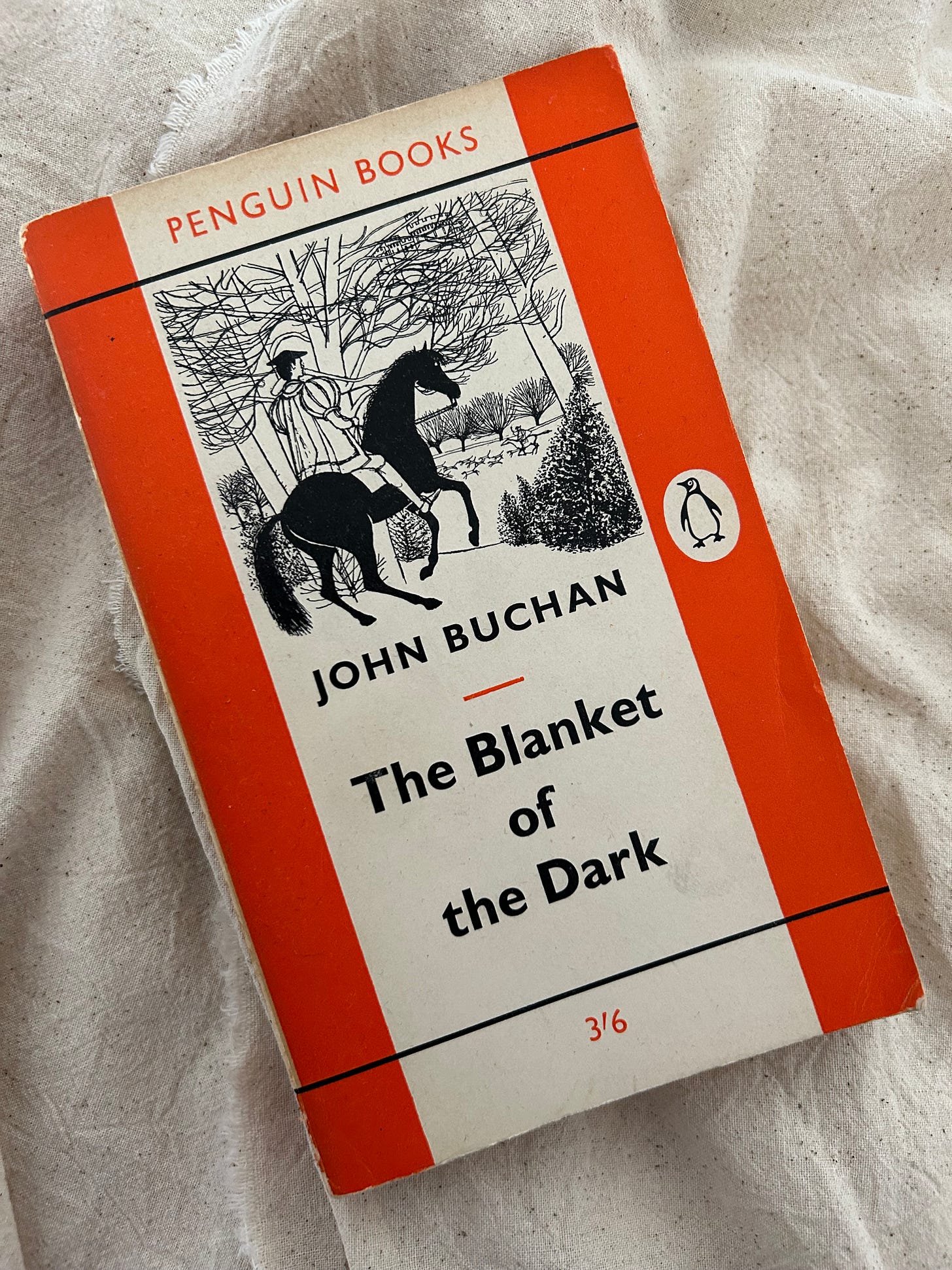 An orange penguin edition of The Blanket of the Dark by John Buchan. The cover features a young man on a horse riding through woodlands, and watching a hunt in the distance.