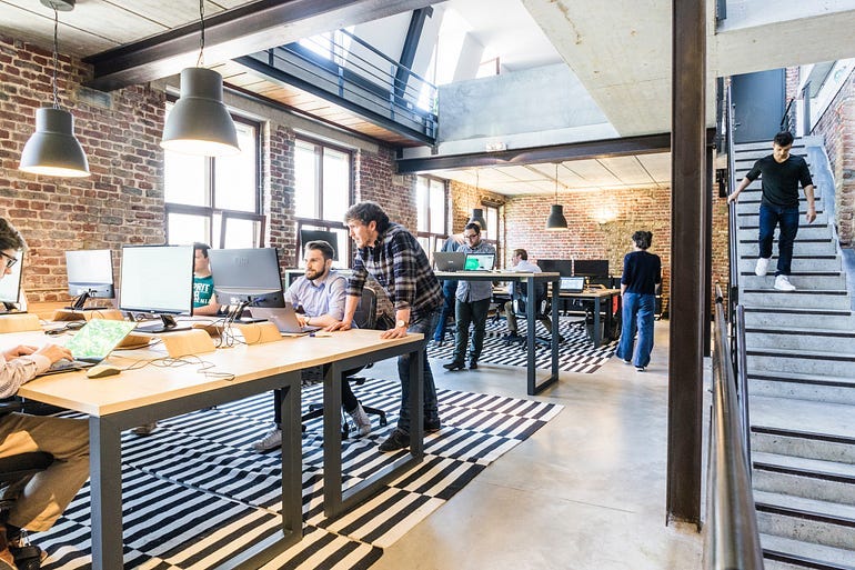 A sample workspace for a startup. There’s open desk layouts, people in casual work outfits, standing tables, and more