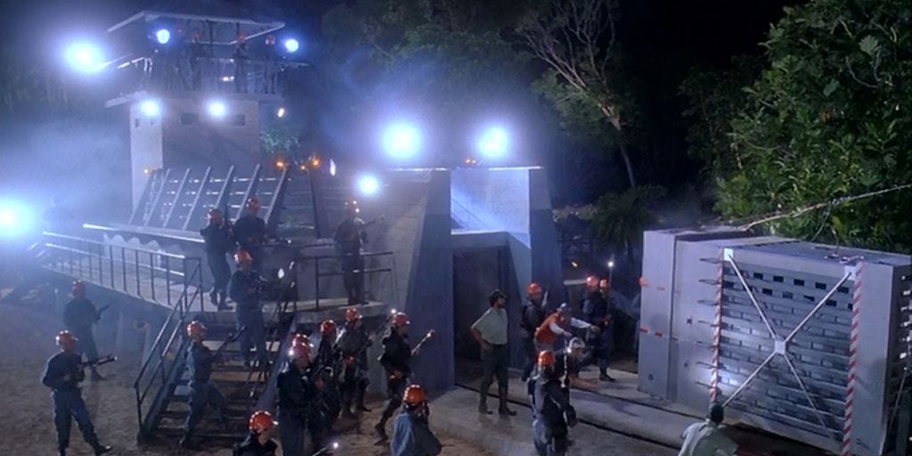 Jurassic Park opening scene. A metal crate is moved towards a modern-looking enclosure. Armed workers are everywhere.  Something dangerous is clearly happening.