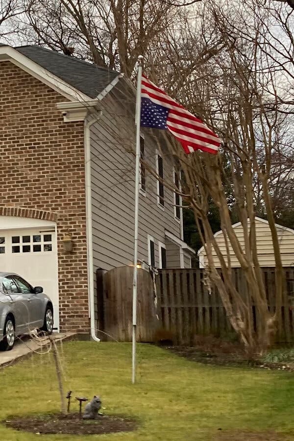 A brick house with an inverted American flag flying over a green suburban lawn. 