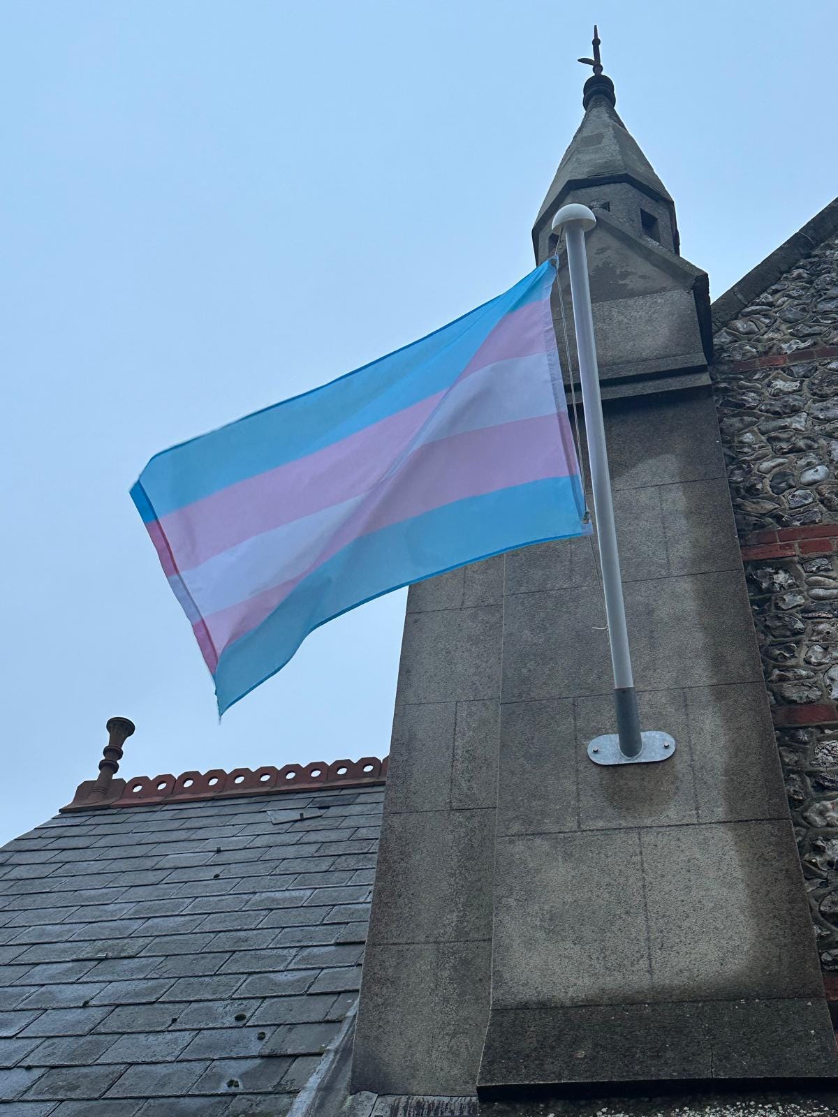 trans flag flies outside old stone sussex church