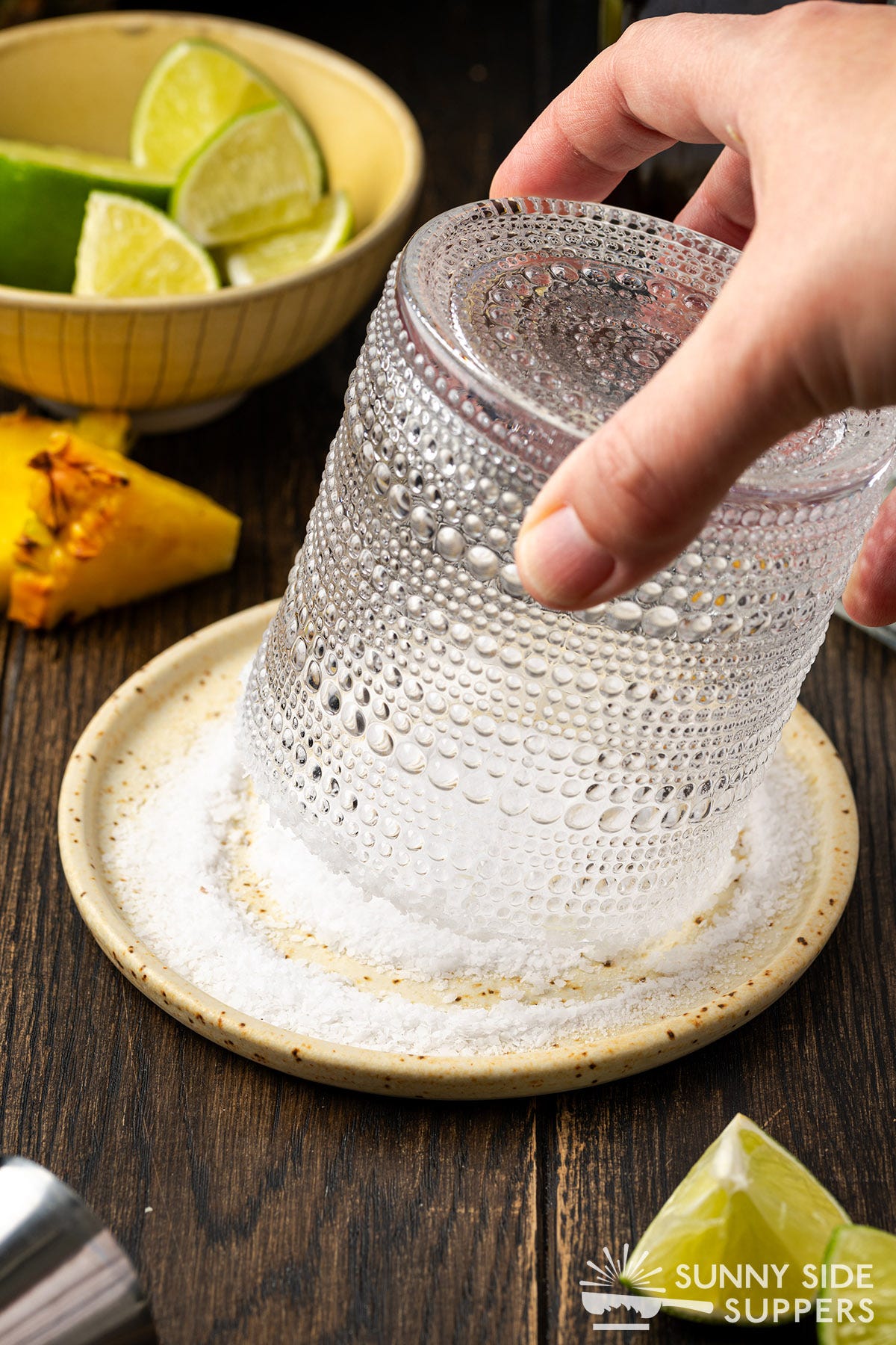 A hand pressing a cocktail a glass into a plate of salt.