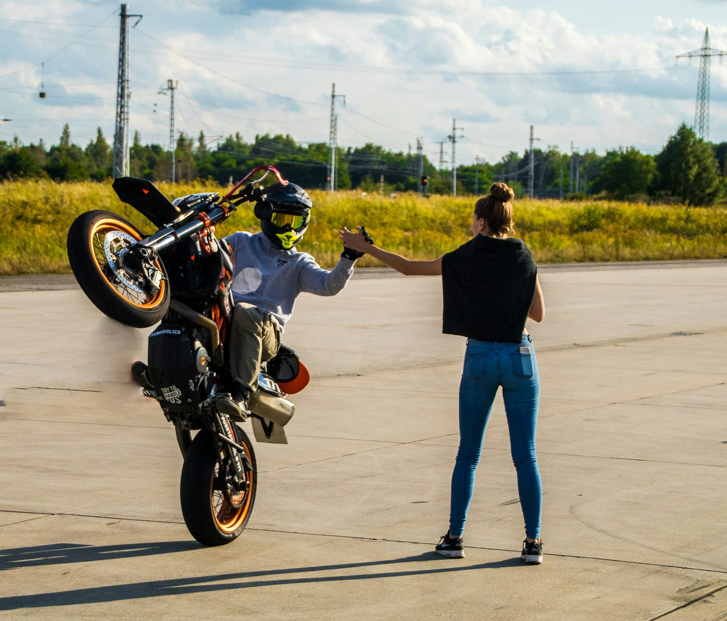 guy popping a wheelie on a motor cycle while high fiving a woman standing (guest writing)