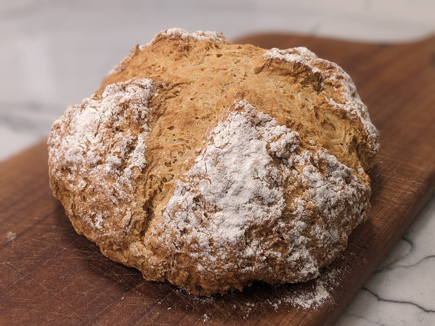 A round loaf of whole wheat soda bread sitting on a walnut cutting board.