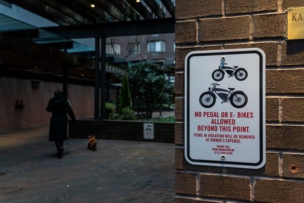 A white rectangular sign prohibiting bicycles is attached to a brick wall in the entry area of an apartment building. 
