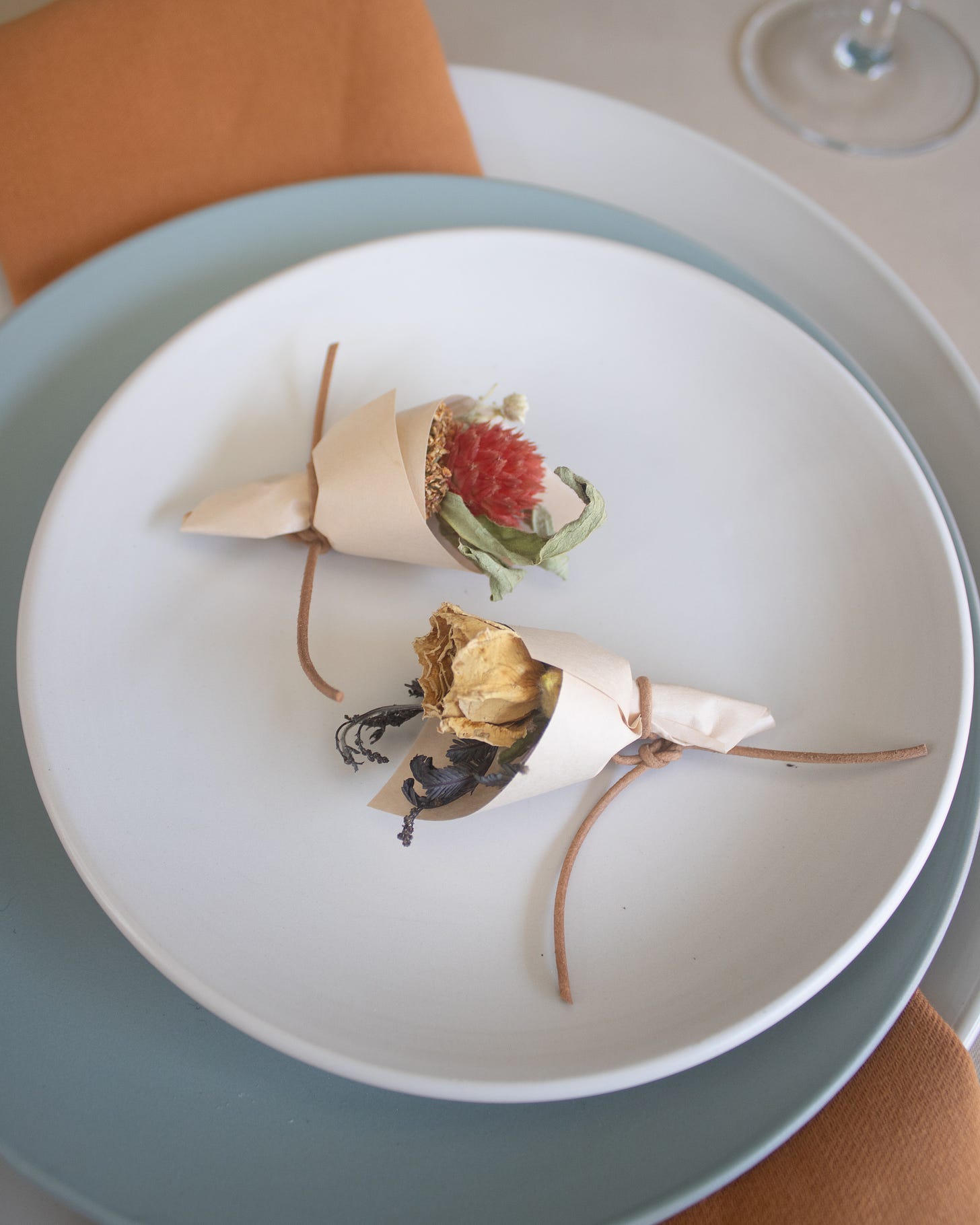 dry flower bouquets wrapped in white paper on a place setting with plates stacked beneath