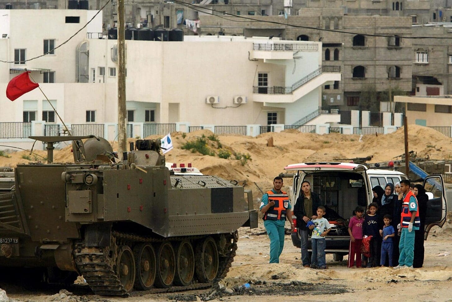 Palestinian medics along with a Palestinian family wait for a permission from Israeli soldiers to cross a blocked street at Tal al-Sultan neighborhood moments after the Israeli army fired a missile on protesters in the southern Gaza Strip town of Rafah, 19 May 2004. At least 10 Palestinians were killed and around 40 wounded in an Israeli helicopter strike on a demonstration to protest a massive army operation there, medical sources and witnesses said. AFP PHOTO/Mauricio LIMA (Photo by MAURICIO LIMA / AFP) (Photo by MAURICIO LIMA/AFP via Getty Images)