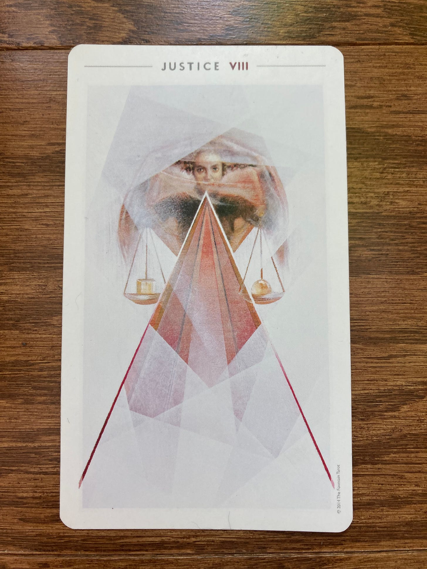 The JUSTICE tarot card lies on a wooden background. The card depicts a woman of color looking at the viewer and holding the scales of justice in front of her