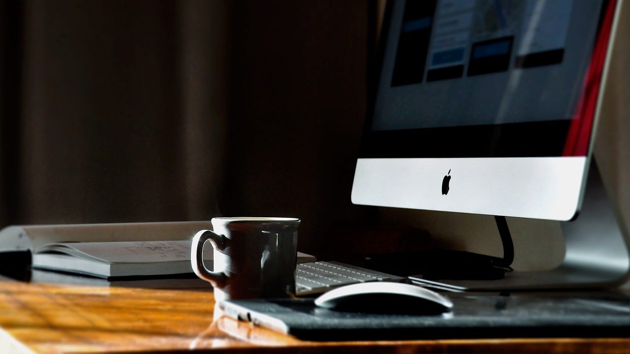 a desk with a computer and a coffee mug, plus an open book