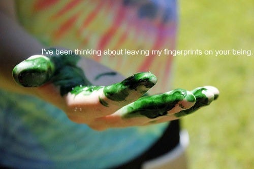 A figure wearing a tie-dye shirt, holding out a hand covered in green paint, with the words "I've been thinking about leaving my fingerprints on your being" written in white font.