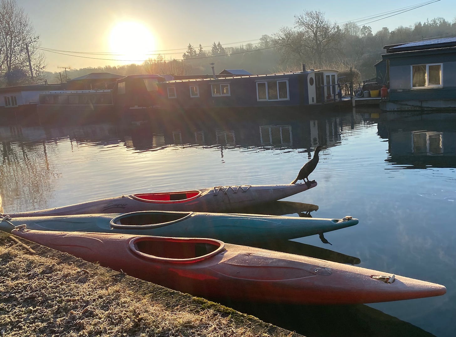 Winter scene with sun setting over canoes by side of canal on waters edge.