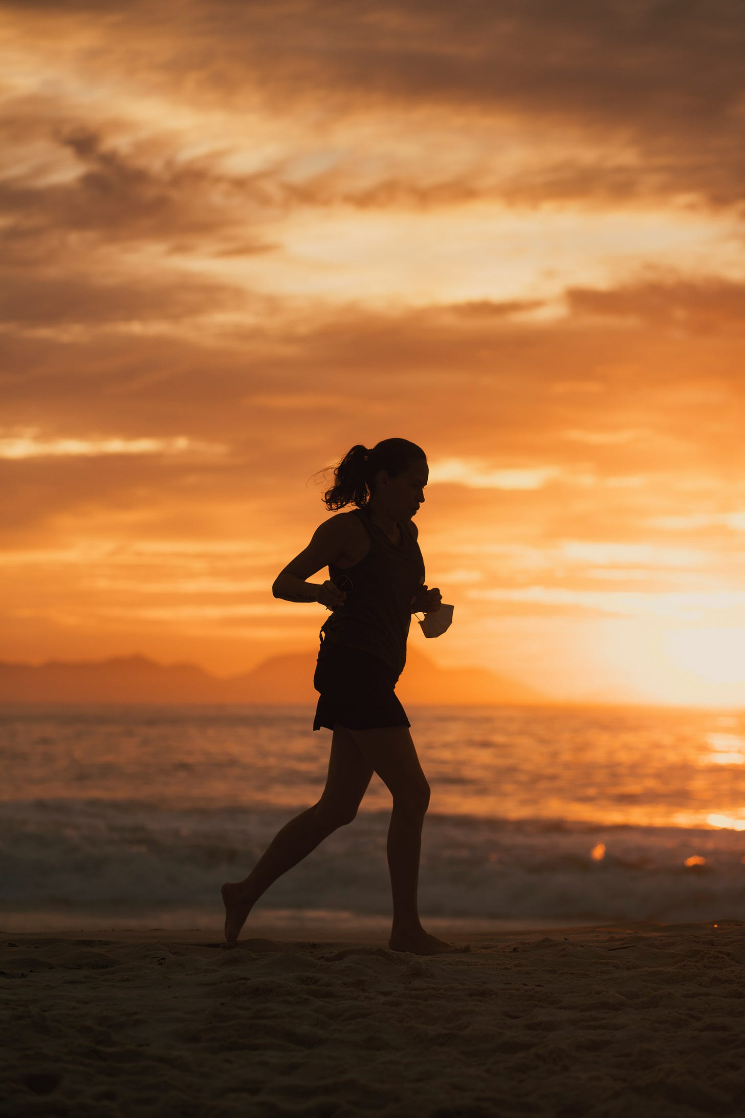 woman running at sunset, barefoot at the beach