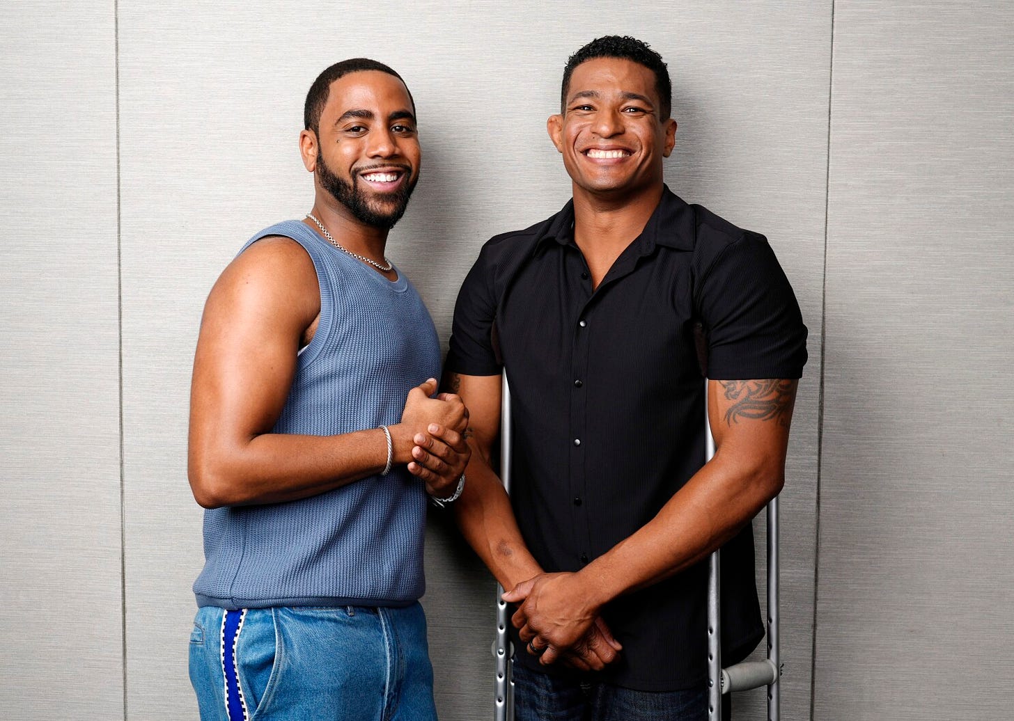 Two men of color are smiling for the camera. One is nondisabled, the other is disabled and uses aluminum crutches.