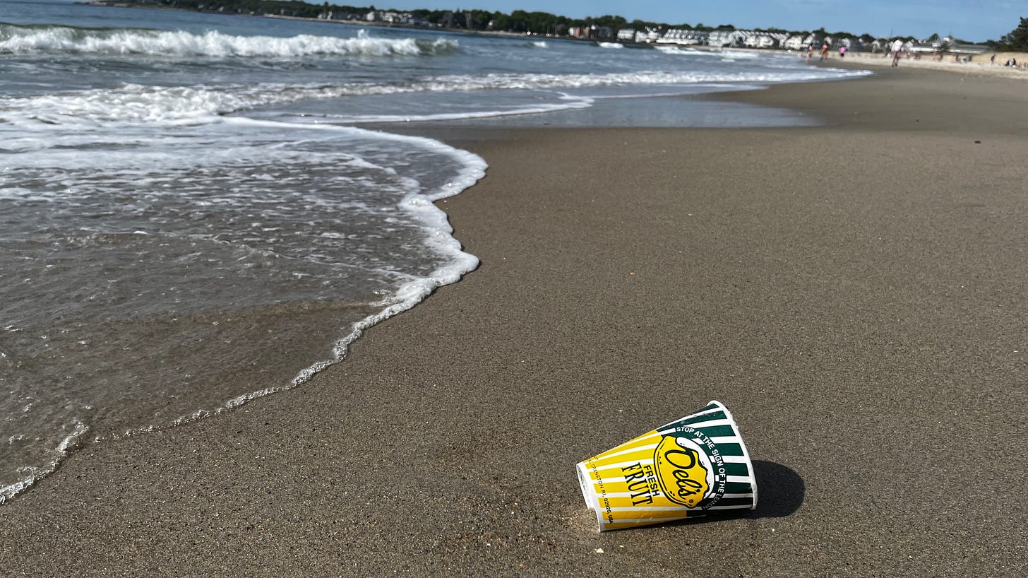 discarded Dels's Lemonade cup on the sand as waves wash up the beach
