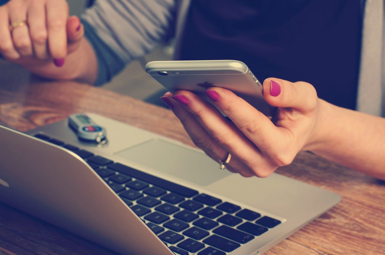 Holding a phone, with MacBook and USB drive on the table.