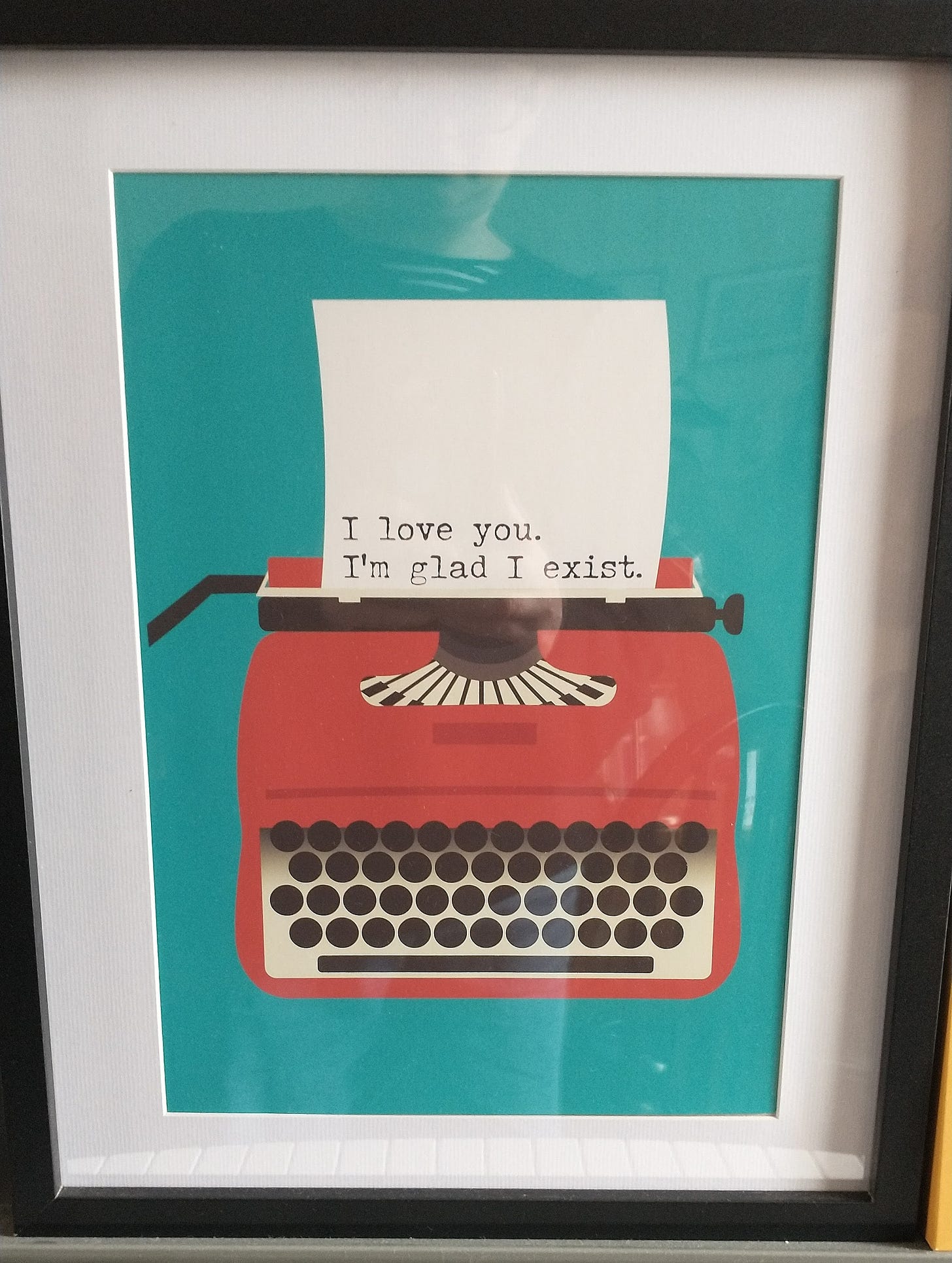 A photo of a framed print: a stylised retro typewriter with 'I love you. I'm glad I exist' as if typed on a sheet of paper sticking out.