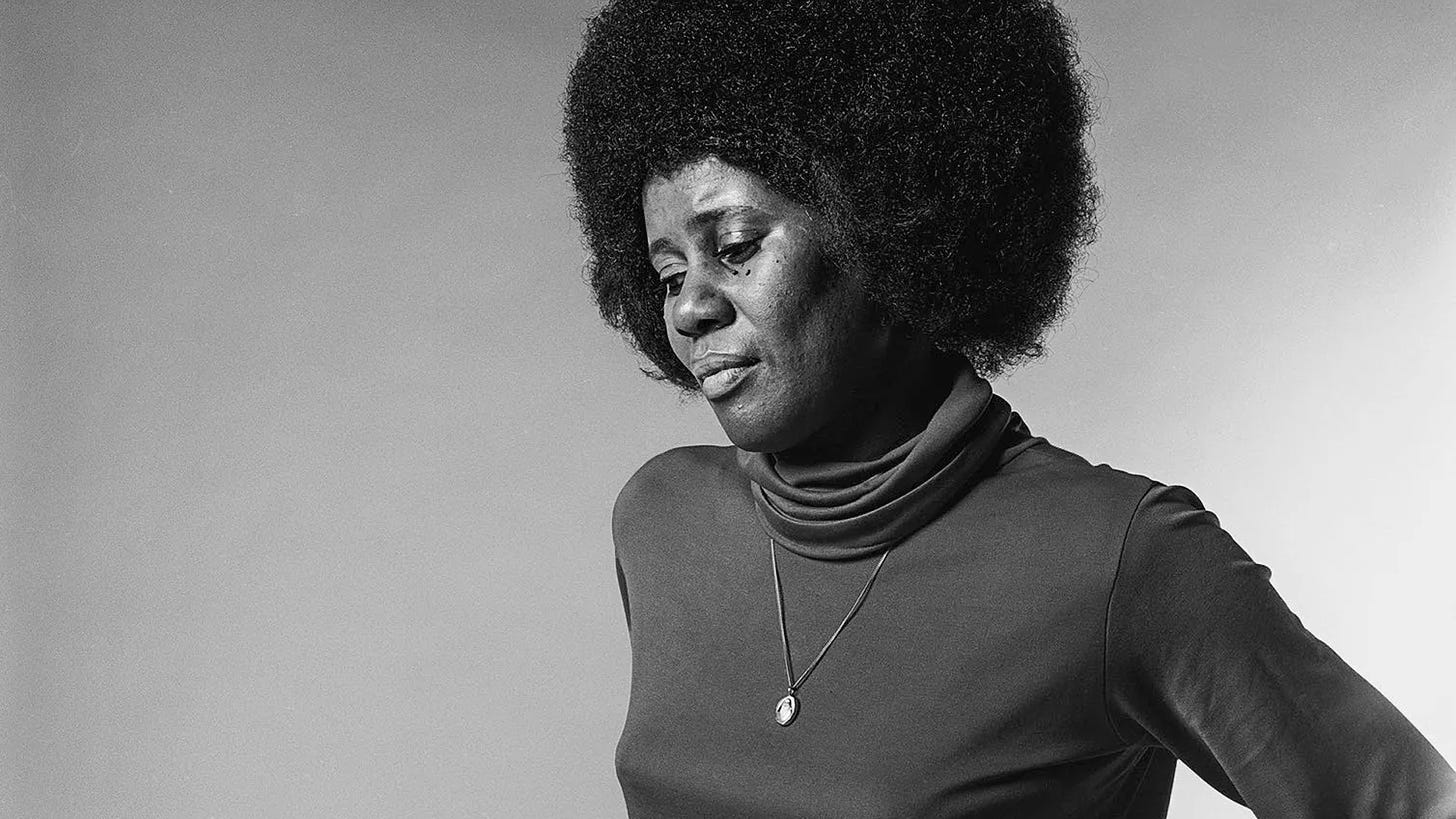 Imagem: Foto de Alice Coltrane, preta e branca, ela jovem, olhando para baixo.