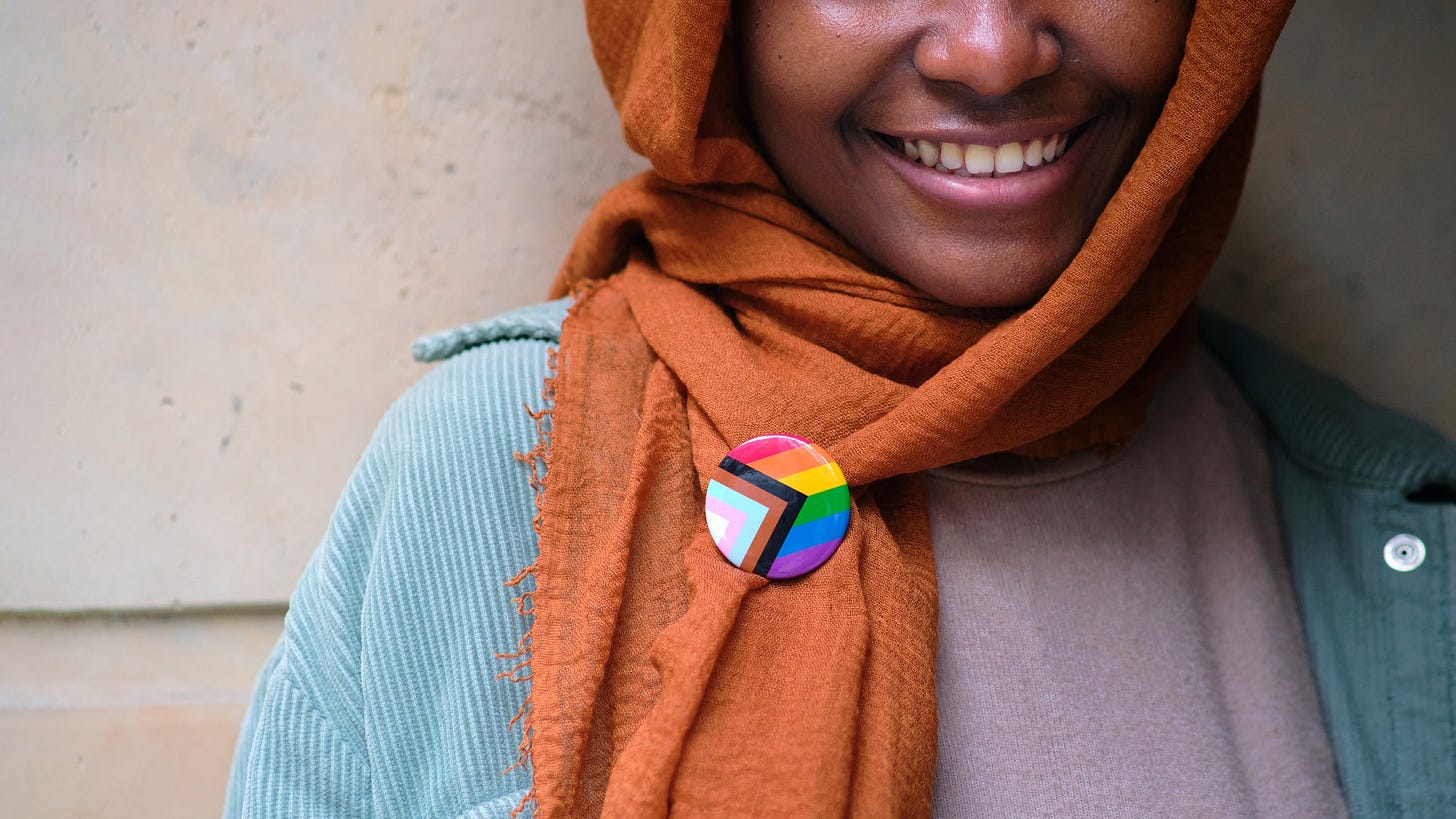 A smiling Muslim woman wearing a lgbtq pin on her clothing