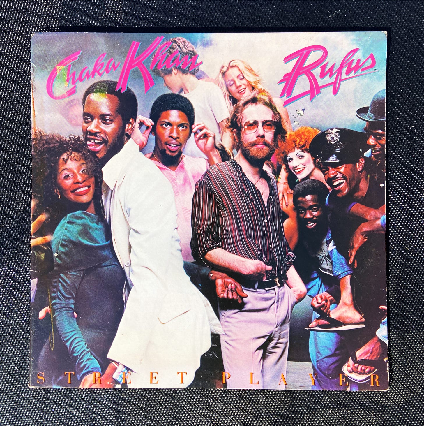 the album cover for my vinyl of Rufus & Chaka Khan's 1978 album Street Player. it features the band front and center, with a cast of characters looming playfully in the background.