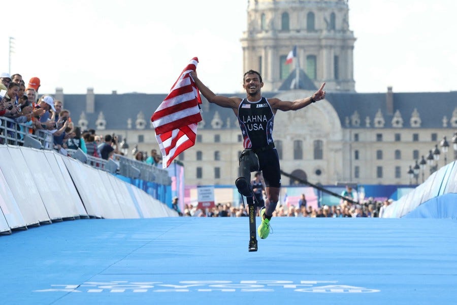 A para-athlete with a leg prosthesis celebrates with an American flag as he crosses a finish line.