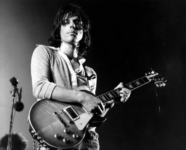A black and white photo of a long-haired young man holding an electric guitar.