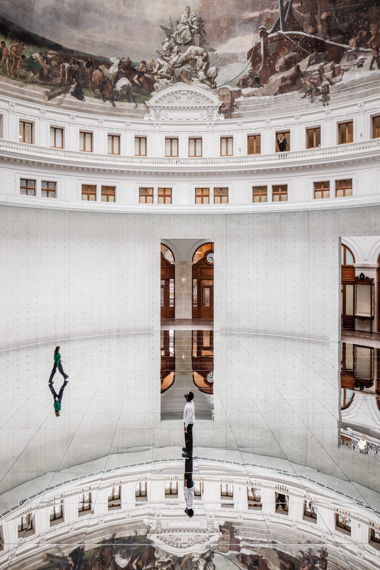 A large rotunda with a mirrored floor, concrete walls, and classical ornamentation on top.