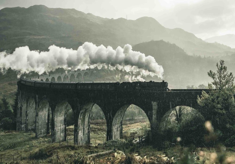 Train billowing steam on an arched trackway on a rainy day in nature