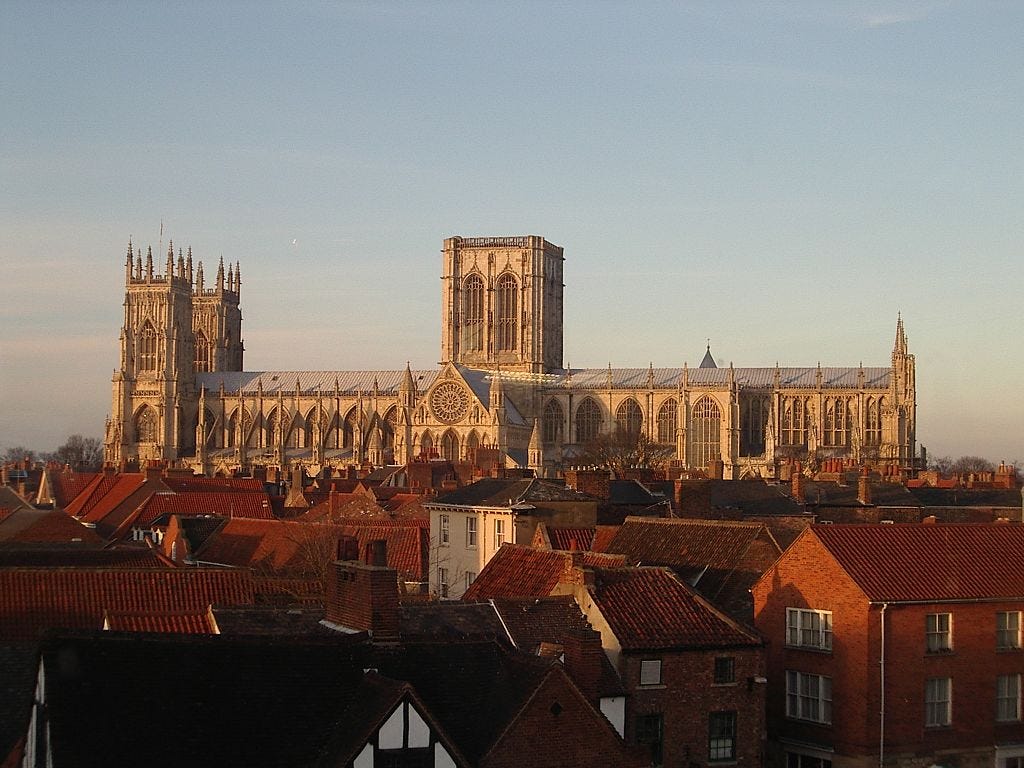 York Minster seen from the side – a long building with a pair of towers at one end and a massive central tower with two perpendicular windows. The round rose window can be seen on the south transept.