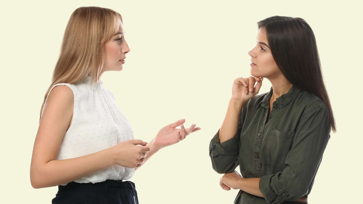 Two women engaged in a conversation, one gesturing while the other listens attentively.