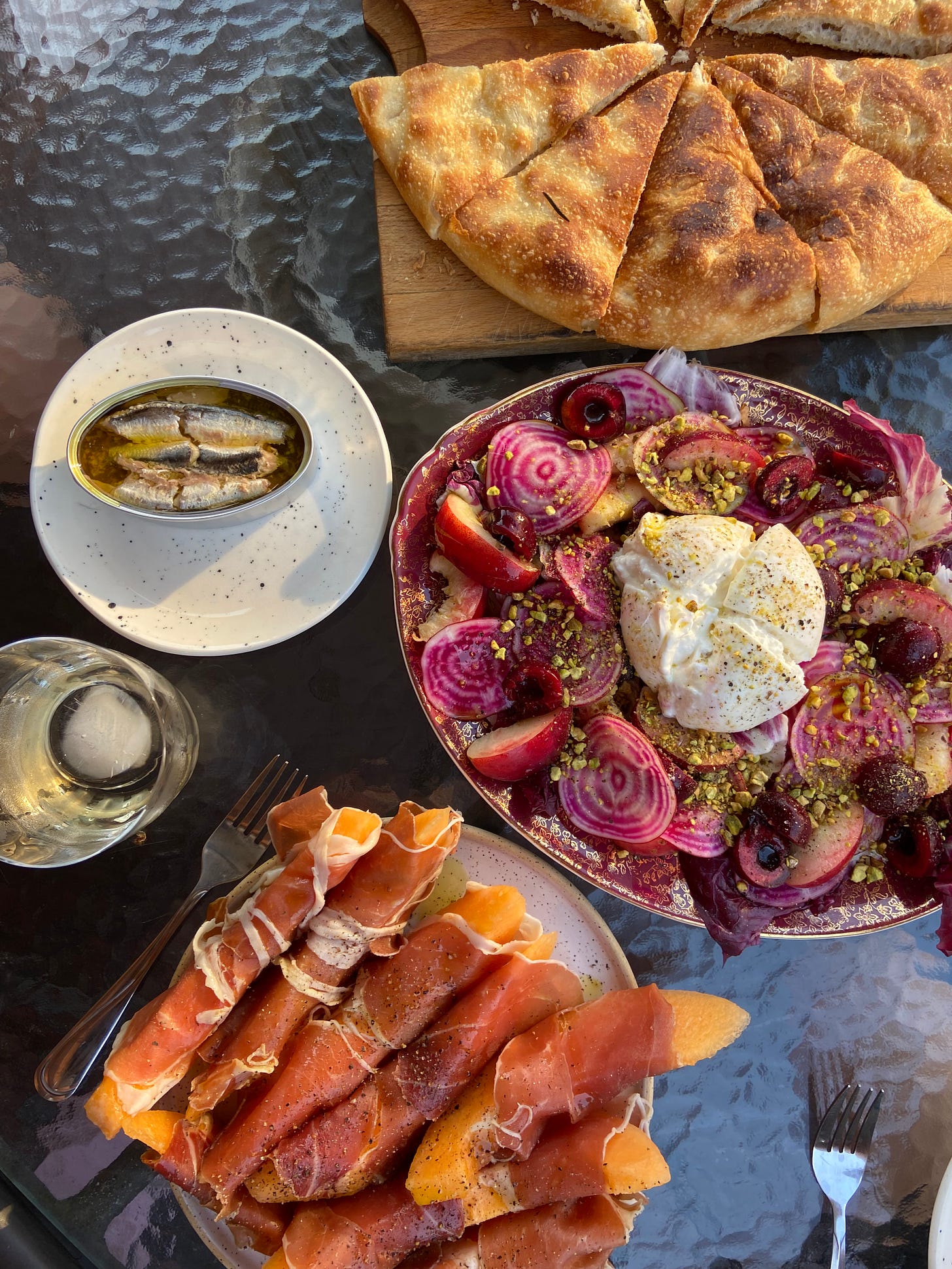 Summer picnic table with sardines, prosciutto with melon, burrata with radishes and apples and a round foccacia