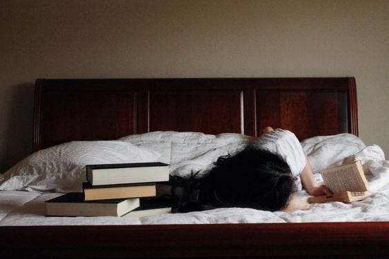 This may contain: a woman laying on top of a bed next to two stacks of books in front of her