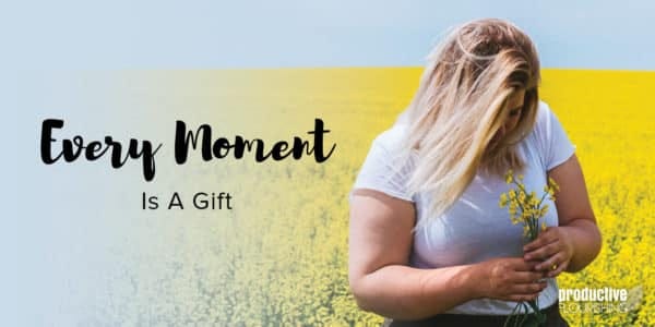 Blonde woman standing in a field of yellow flowers, smelling a flower. Text overlay: Every Moment Is A Gift
