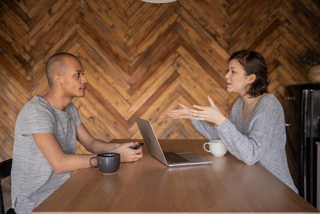 two people talking face to face across a wooden table