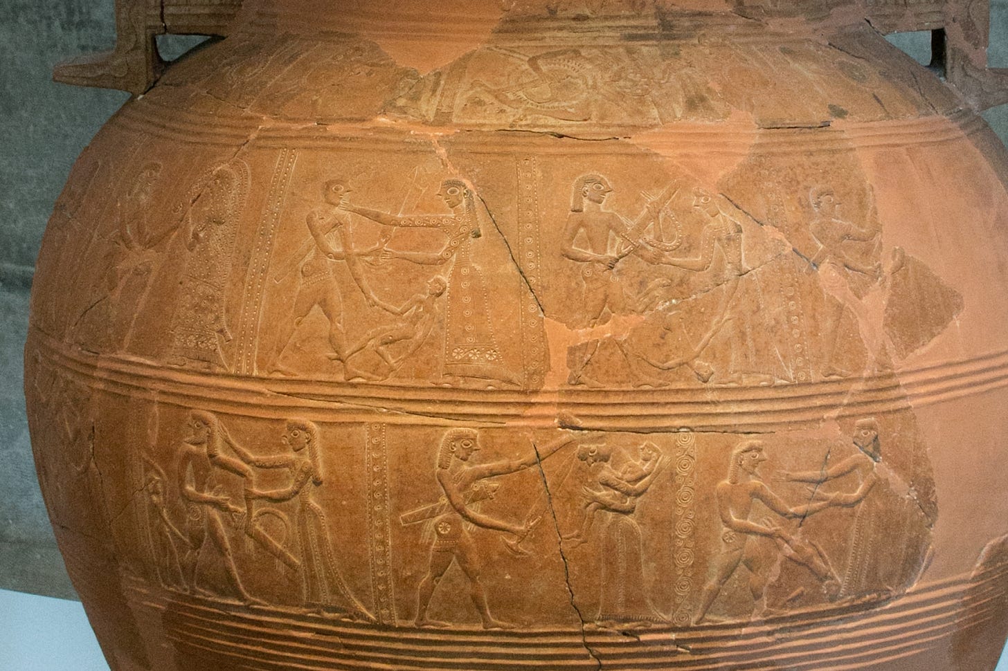 Photograph of a figured panel from a clay vase showing a warrior swinging an infant in a sequence 